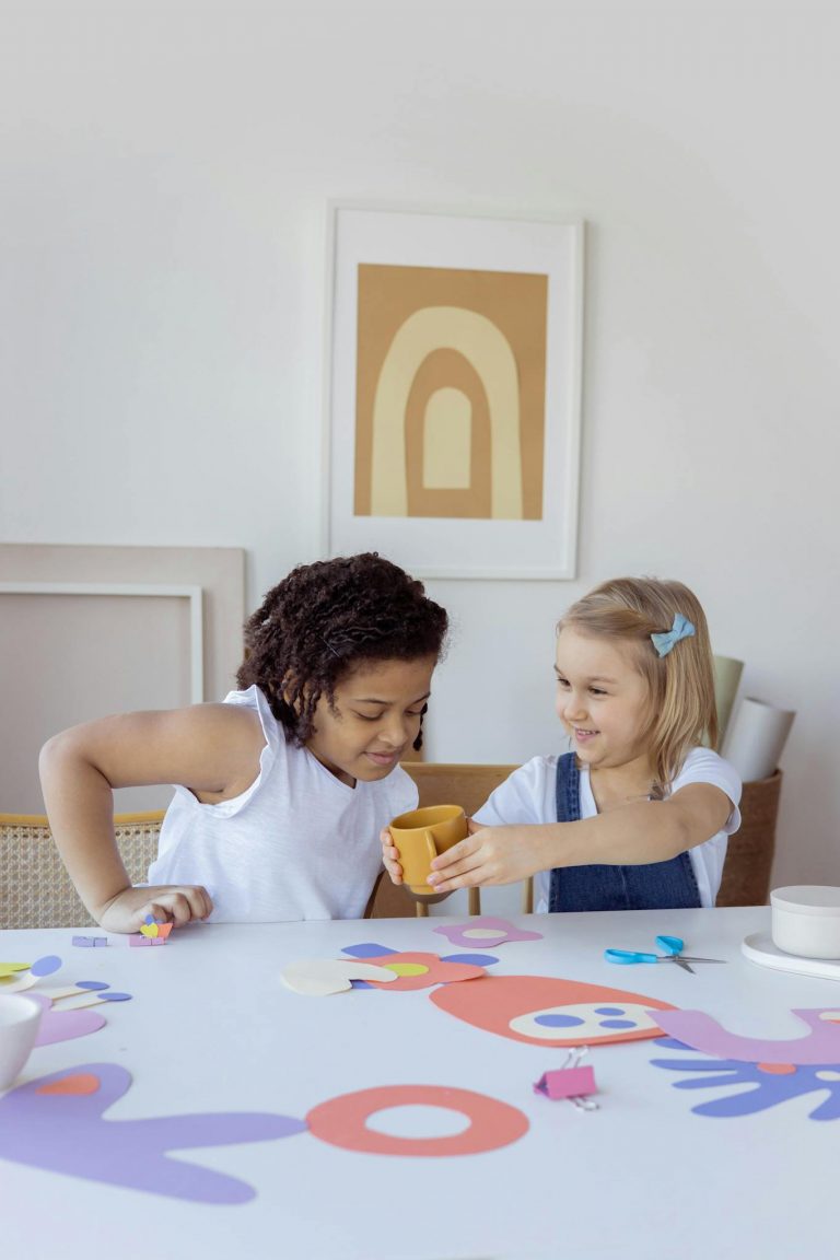 Two girls engaging in arts and crafts, sharing creative moments at a table indoors.